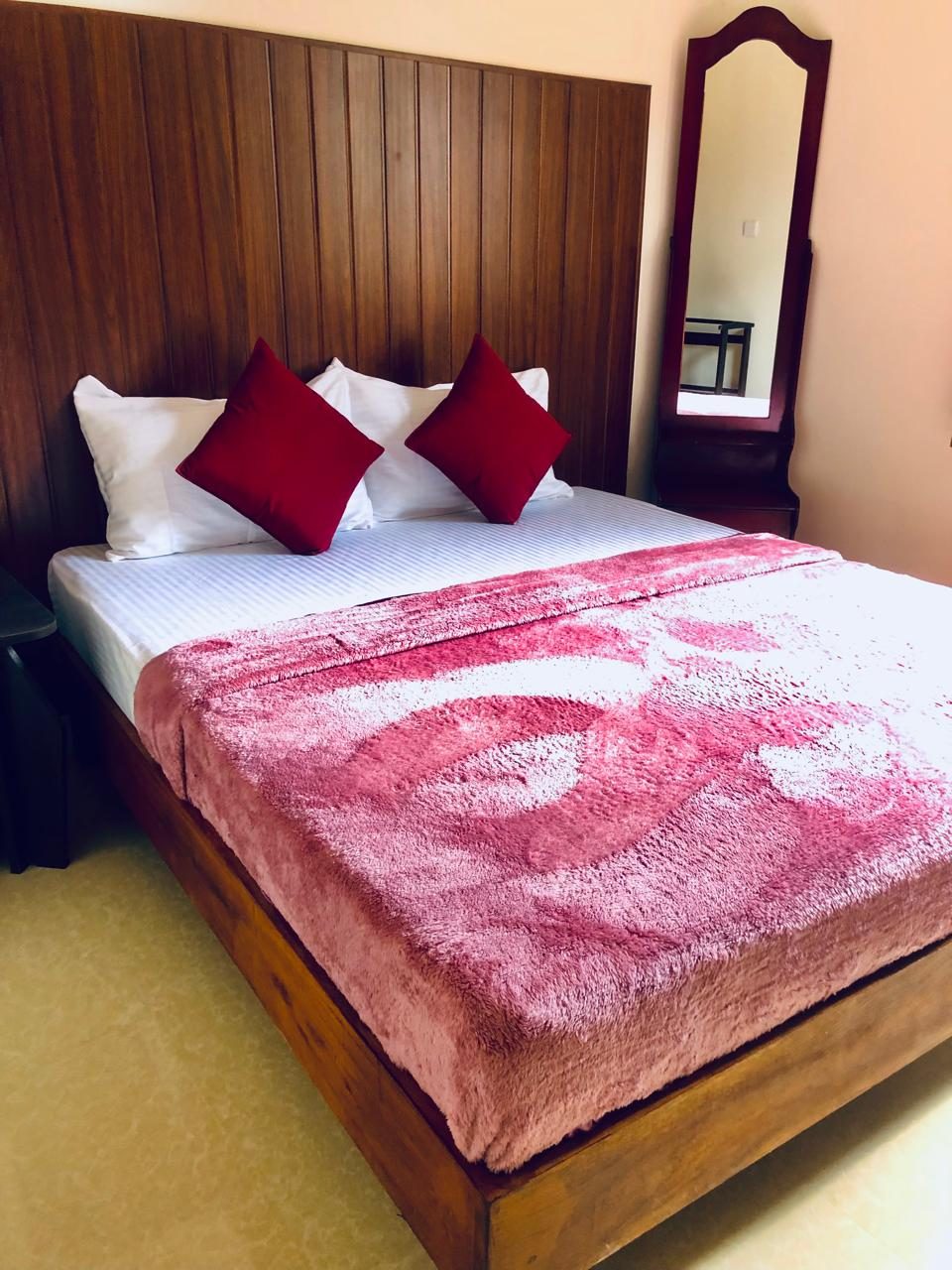 Deluxe Double Room bed with a pink cover and a mirror